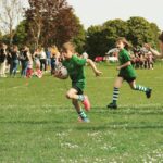 Zwei Kinder in grünen Trikots von Rugby Trier, die gerade Rugby spielen.